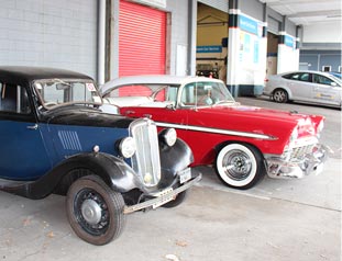 Two classic cars parked outside mechanics