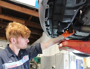 Young mechanic inspecting under car on lift